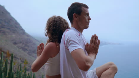 Mit-Dem-Ozean-Als-Leinwand-Meditieren-Ein-Mann-Und-Eine-Frau-Auf-Einem-Bergfelsen-Und-Praktizieren-Yoga,-Ihre-Rücken-Berühren-Sich-Und-Sie-Finden-Ruhe